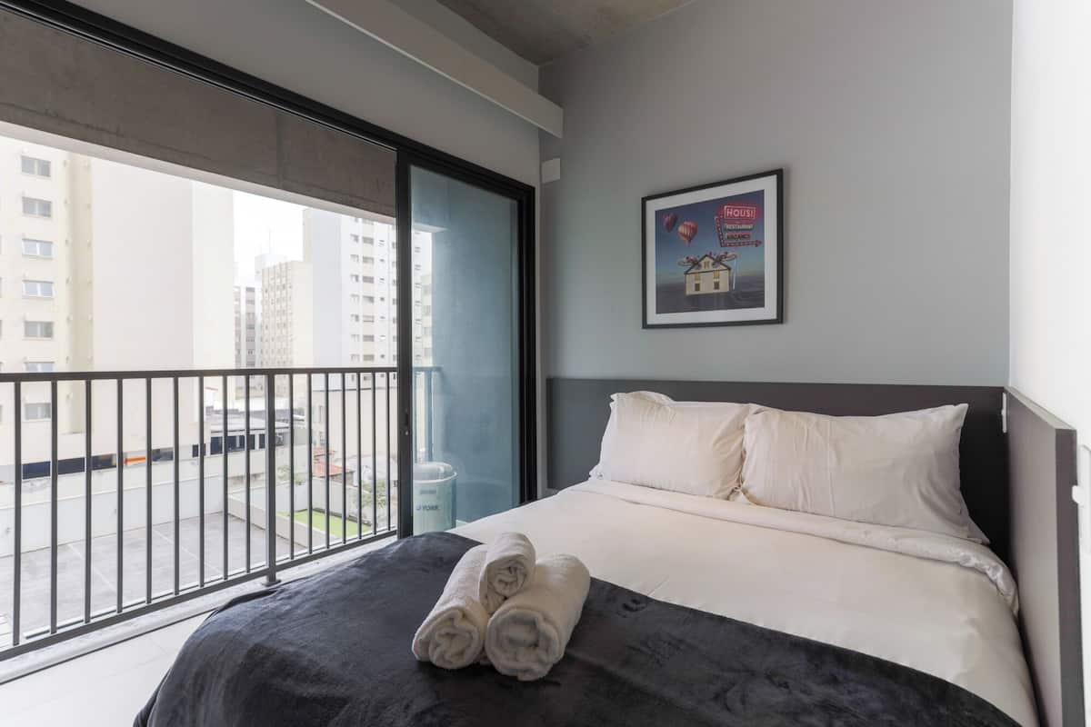 Une chambre d’hôtel avec un lit, une grande fenêtre et un tableau encadré au mur.