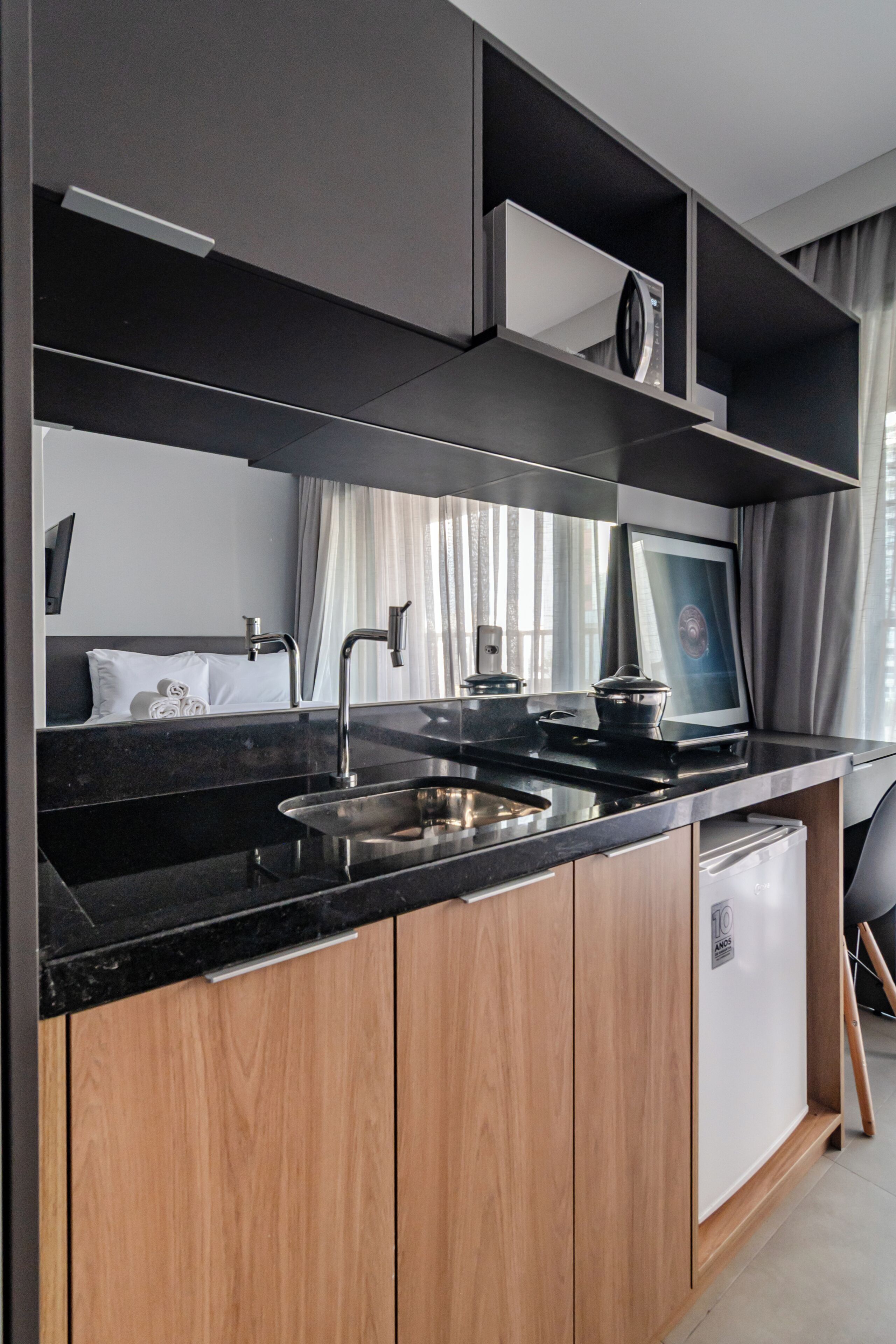 A modern kitchen with a black countertop, wooden cabinets, a built-in oven, and a small refrigerator.