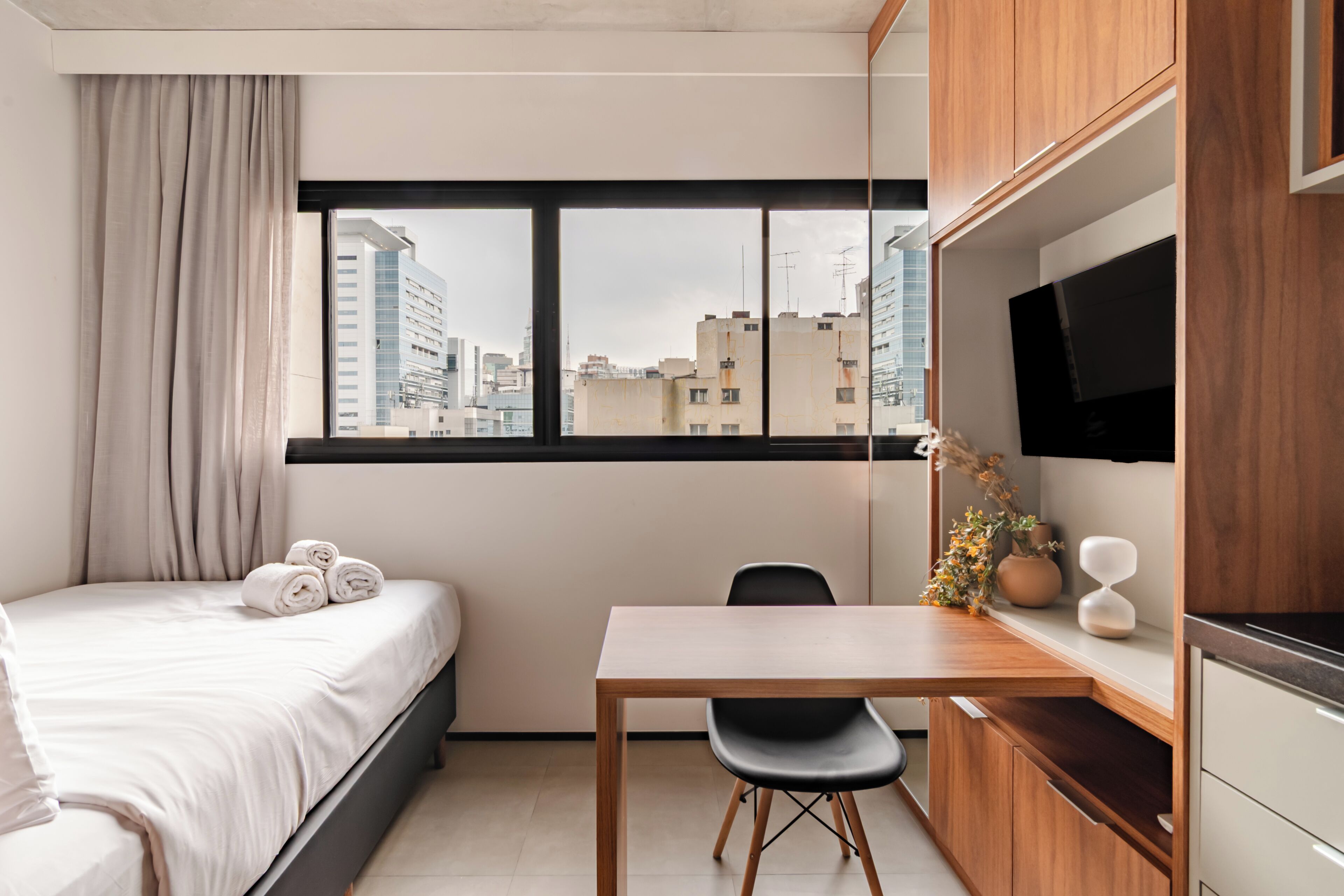 Una habitación de hotel moderna con cama, escritorio, silla, televisión y ventana con vista a la ciudad.