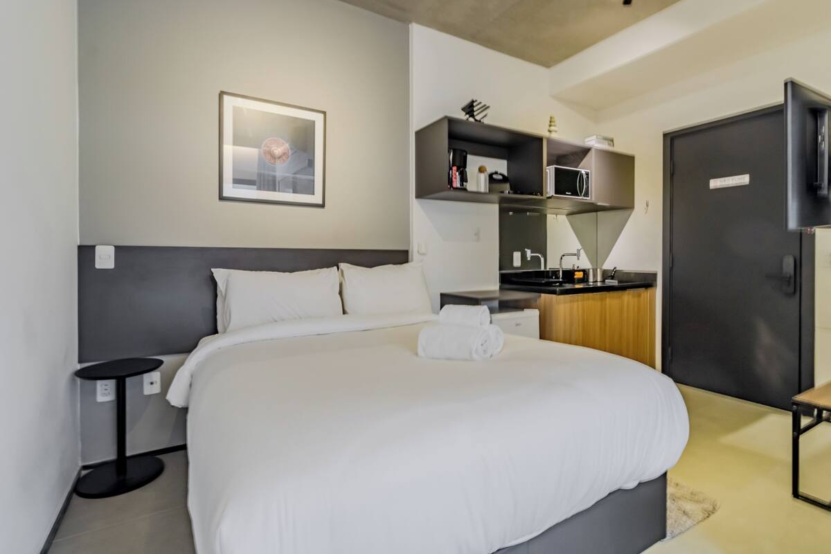 Une chambre d’hôtel moderne dotée d’un grand lit, d’une petite table ronde, d’un coin cuisine intégré et d’un téléviseur.