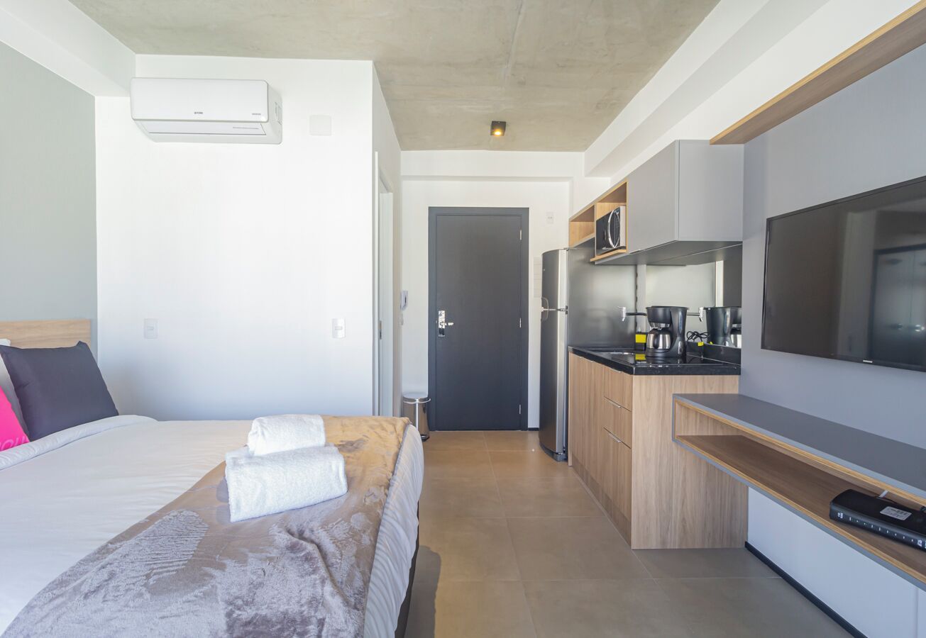 Una habitación de hotel moderna con una cama, un televisor, una kitchenette y una puerta que da a otra habitación.