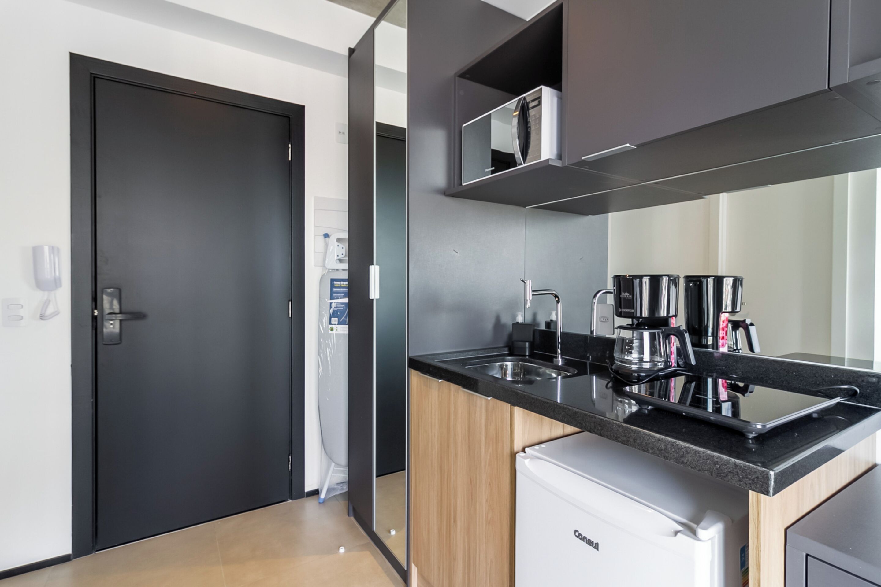 A modern kitchen with a black countertop, a coffee maker, and a refrigerator.