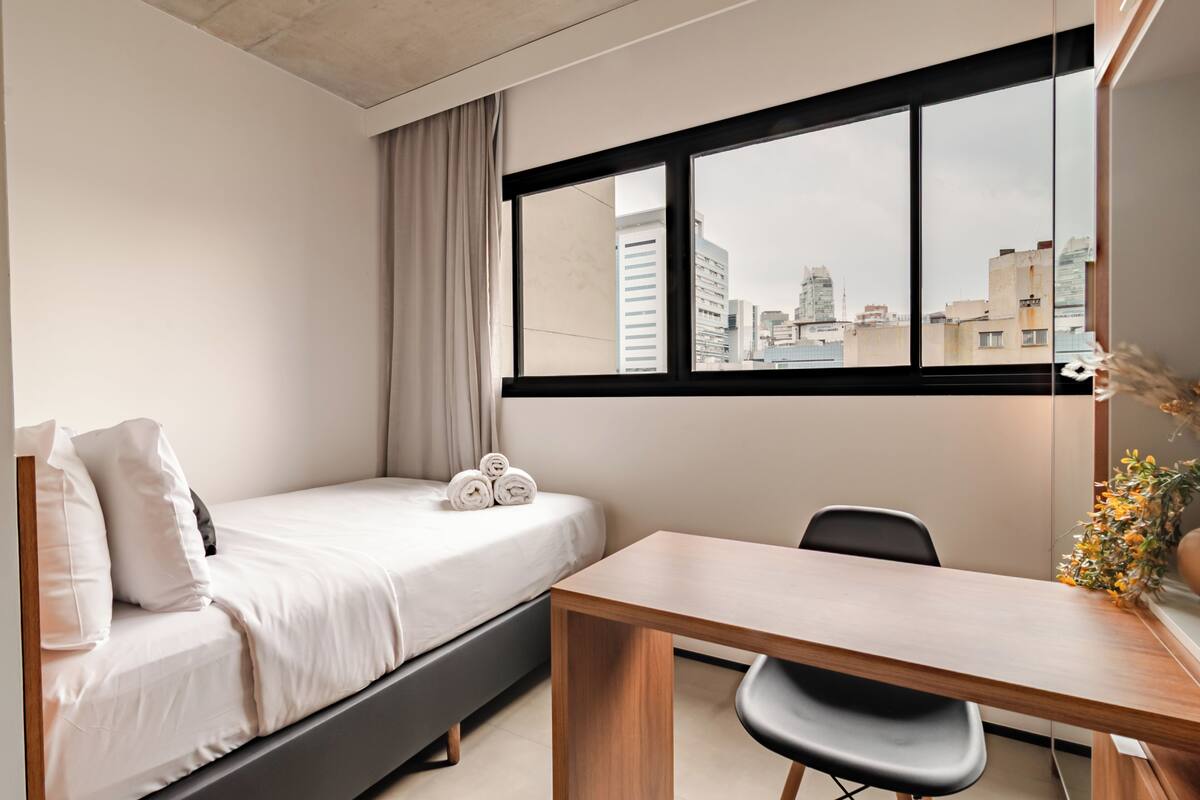 Une chambre à coucher avec un lit, un bureau et une fenêtre donnant sur la ville.