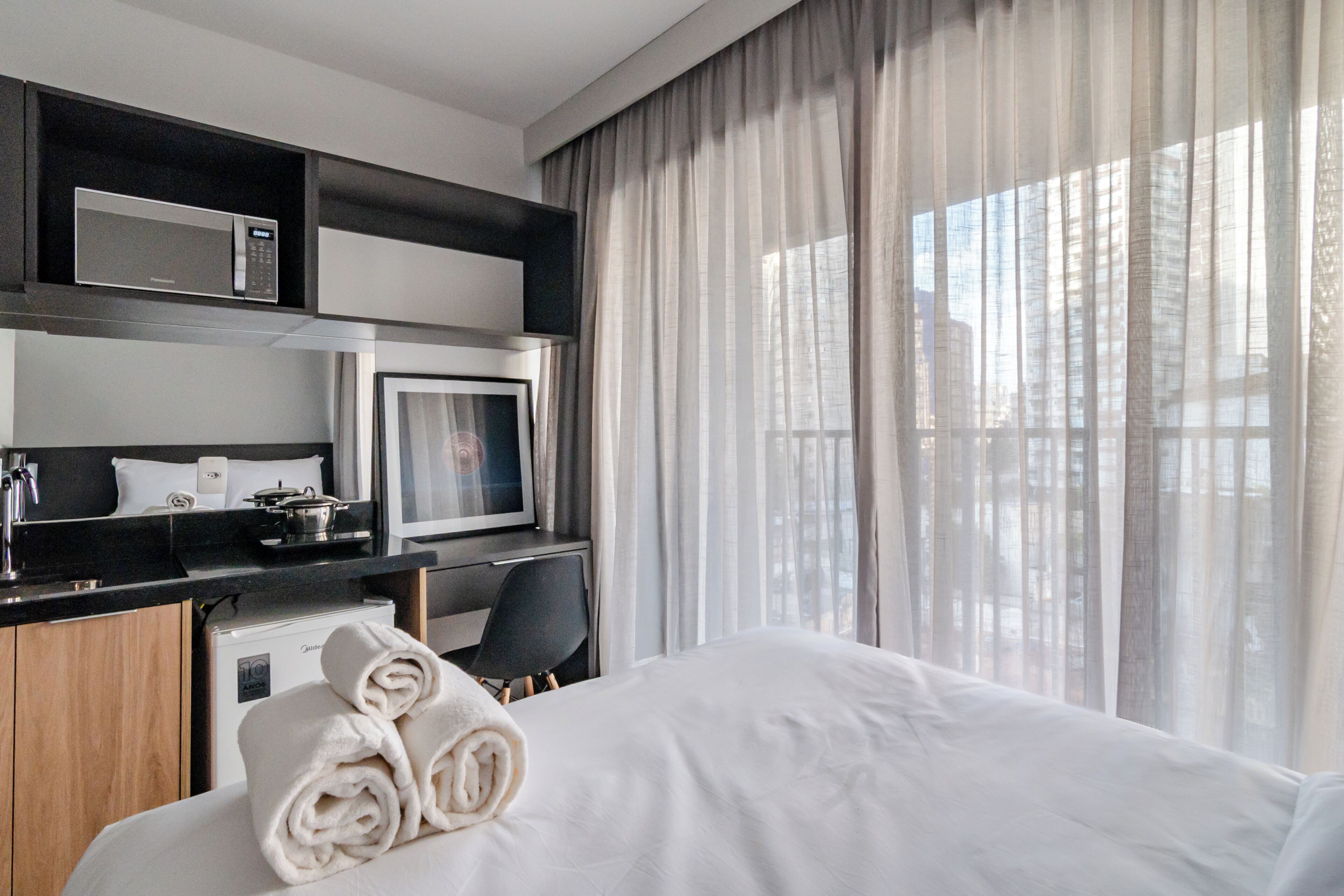 A hotel room with a bed, a desk with a computer, a microwave, and a refrigerator.