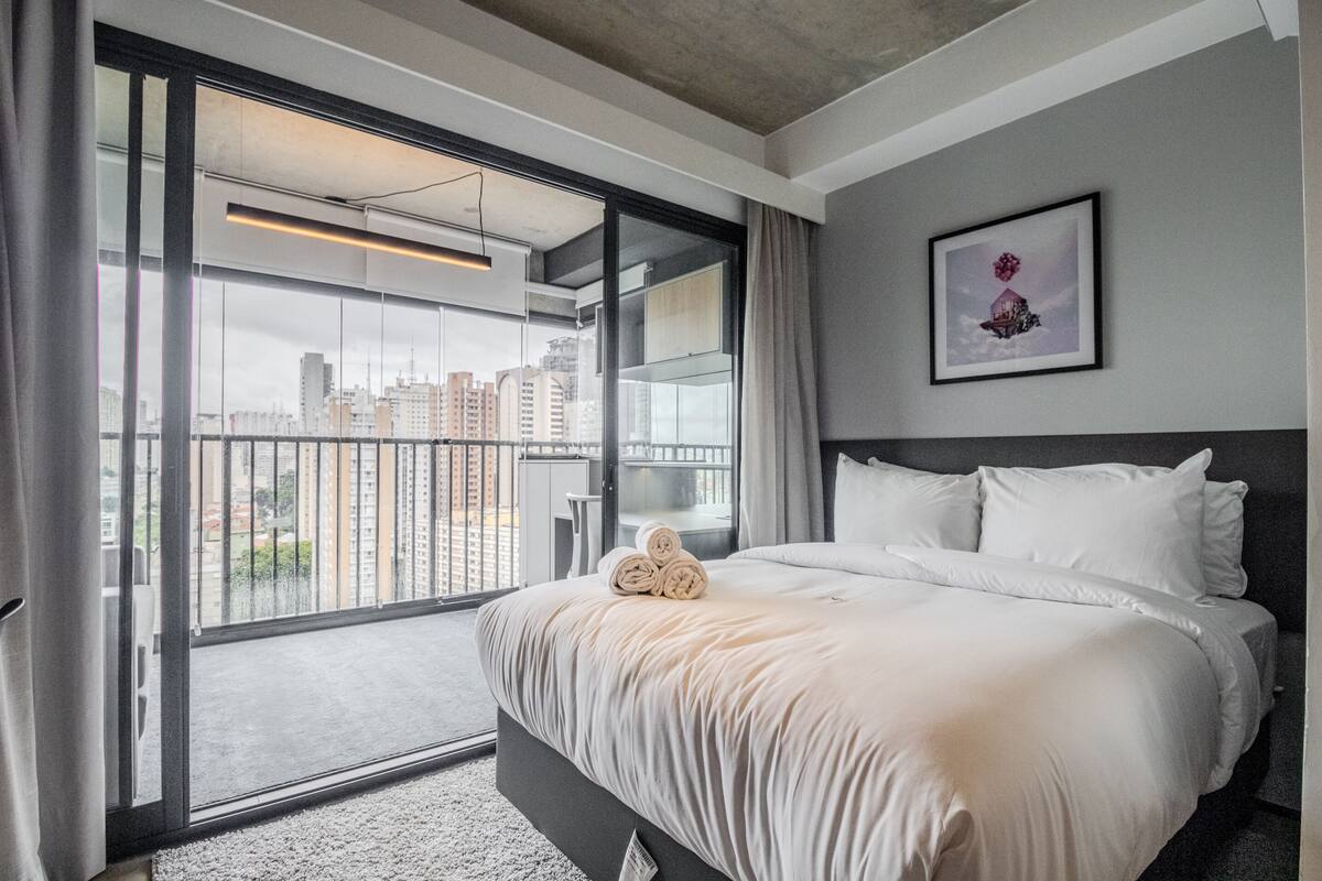Une chambre d’hôtel avec un grand lit, une vue sur la ville grâce à une porte-fenêtre coulissante et un tableau encadré au mur.