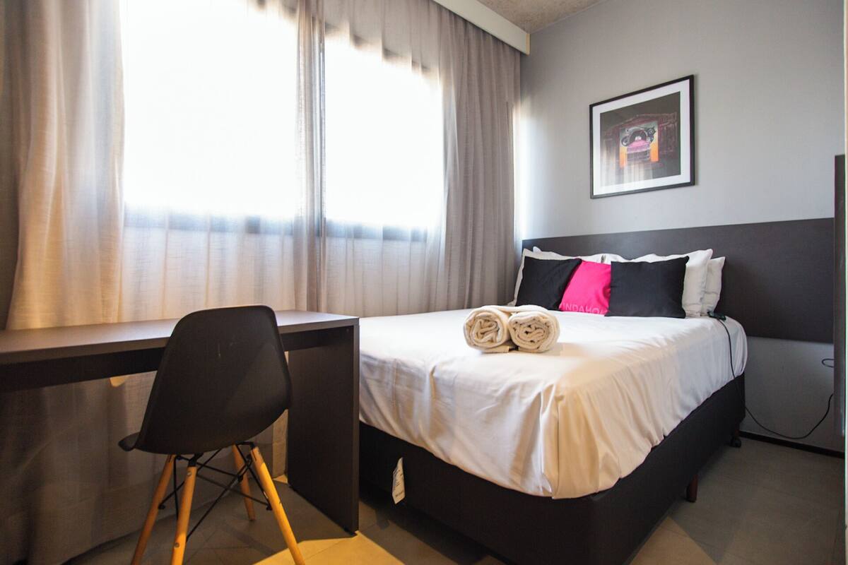 Une chambre d’hôtel avec un lit, un bureau, une chaise et une fenêtre avec des rideaux.