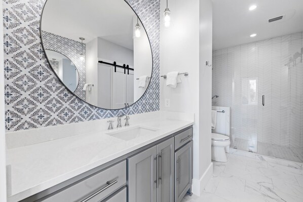 A modern bathroom with a large mirror, a white sink, and a shower area.