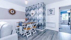 A modern dining area with a geometric-patterned accent wall, a dining table with chairs, and a pendant light.