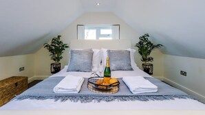 Une chambre à coucher avec un lit, une fenêtre, deux plantes en pot, une bouteille de champagne et un panier de fruits.
