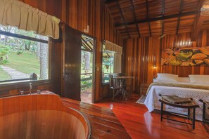 A wooden cabin interior with a wooden bathtub, a bed with white bedding, and a dining area with a table and chairs.
