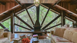 A cozy reading nook with a fireplace, books, and a view of the forest through large windows.
