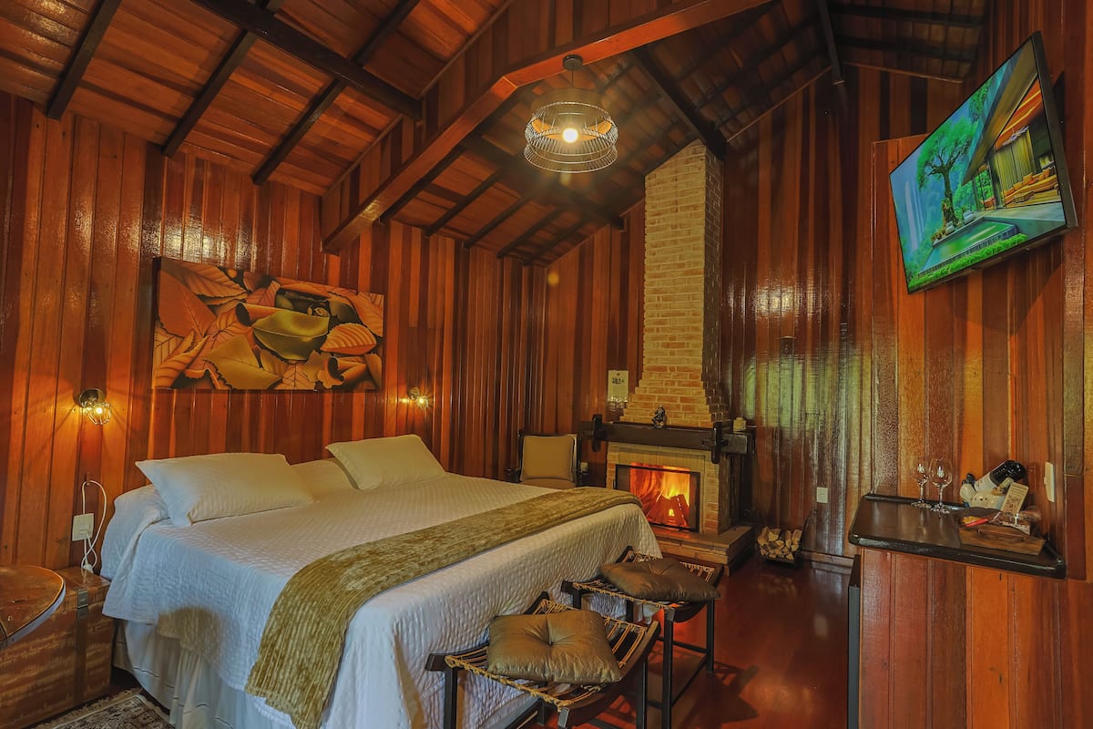 A cozy room with a large bed, a fireplace, wooden walls, and a painting on the wall.