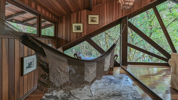 A hammock in a wooden room with large windows, framed pictures on the walls, and a hanging light fixture.