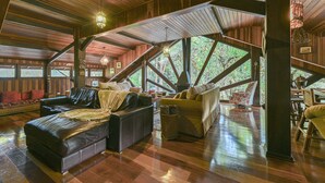 A spacious loft-style room with a high ceiling, wooden beams, and large windows offering views of the outdoors. - Pousada Cantos e Contos (Camanducaia)