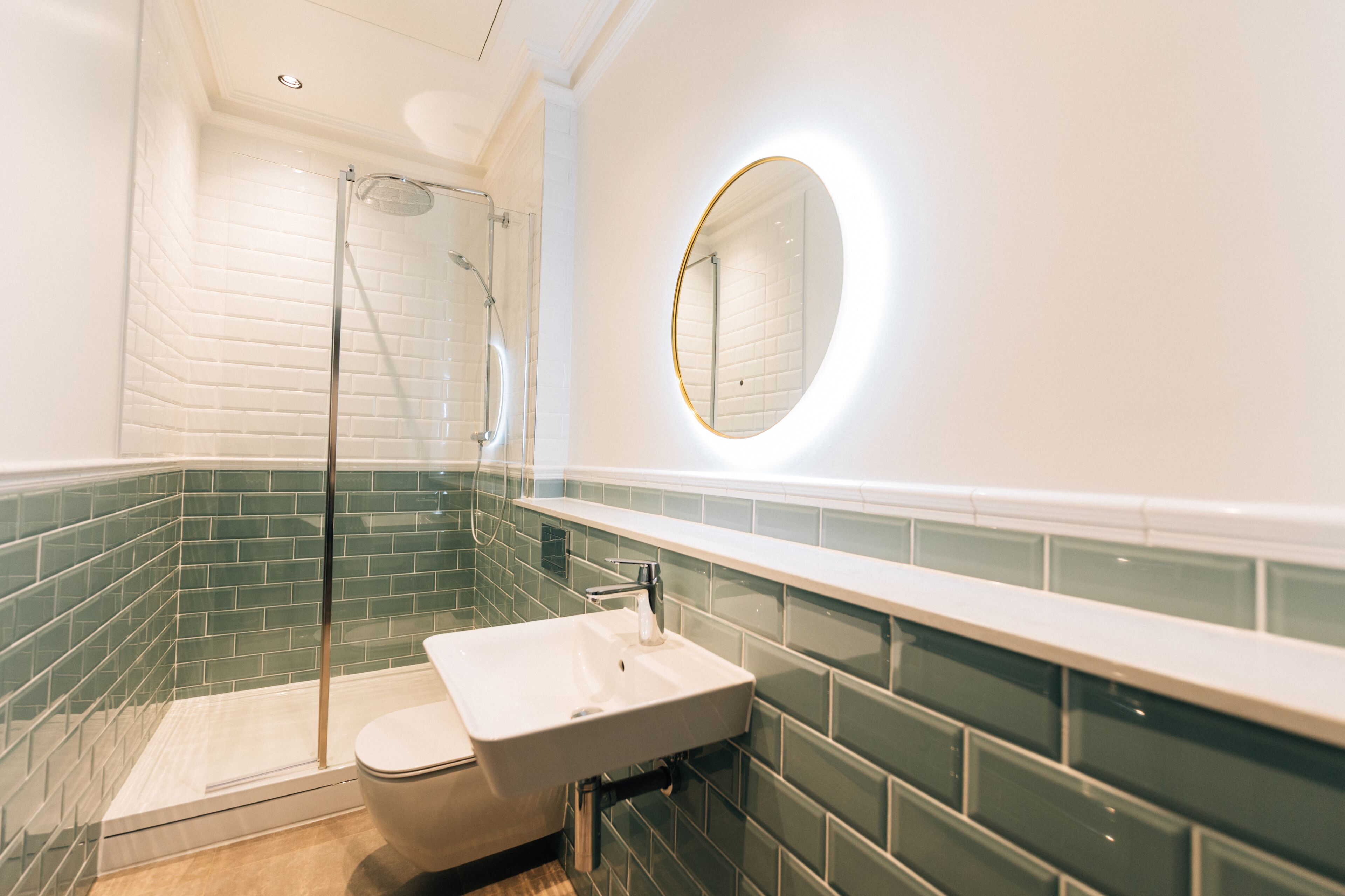Un baño moderno con cabina de ducha de vidrio, un lavabo blanco y un espejo redondo con marco dorado.