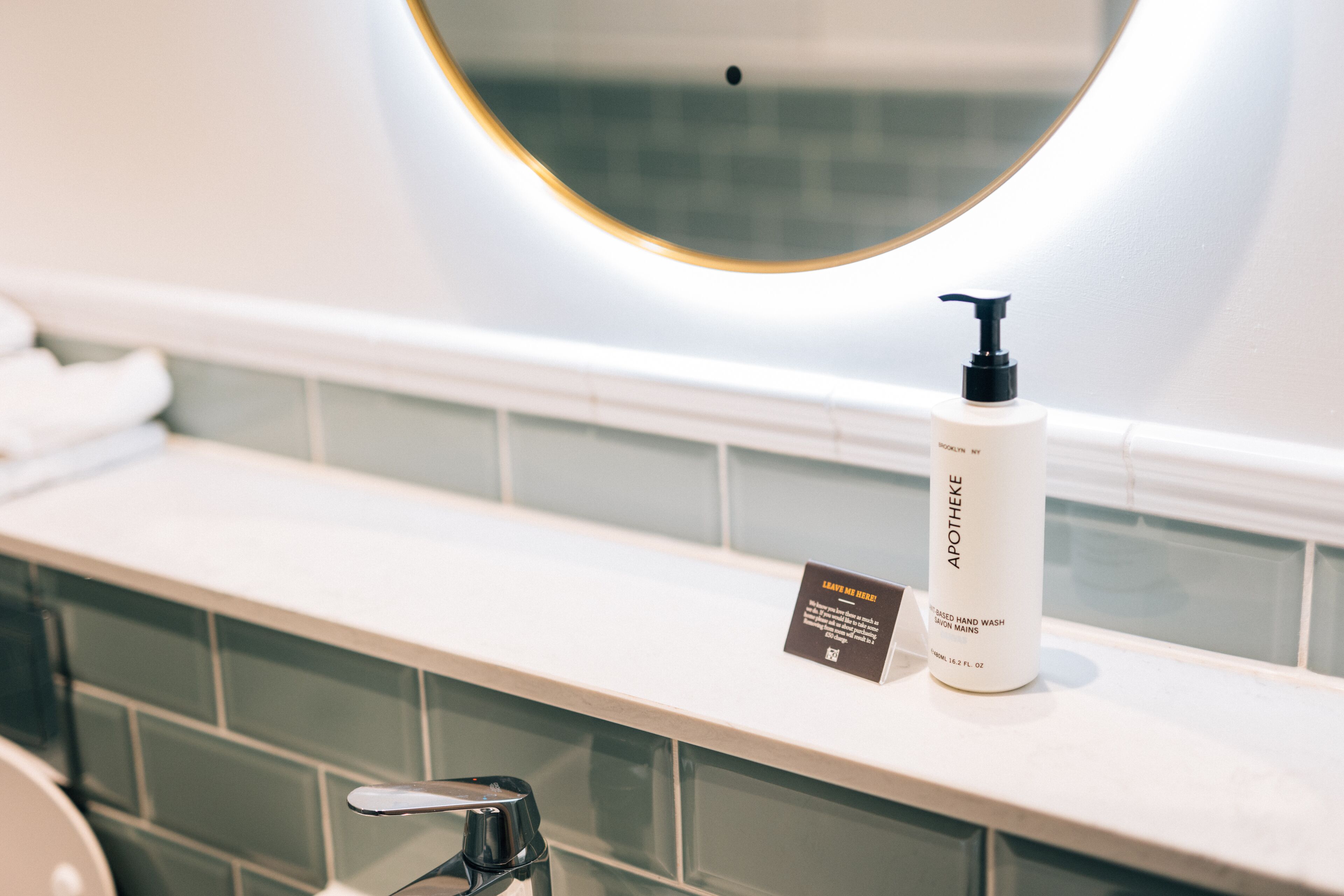 A bathroom with a white sink, a bottle of hand wash soap, and a mirror above the sink.