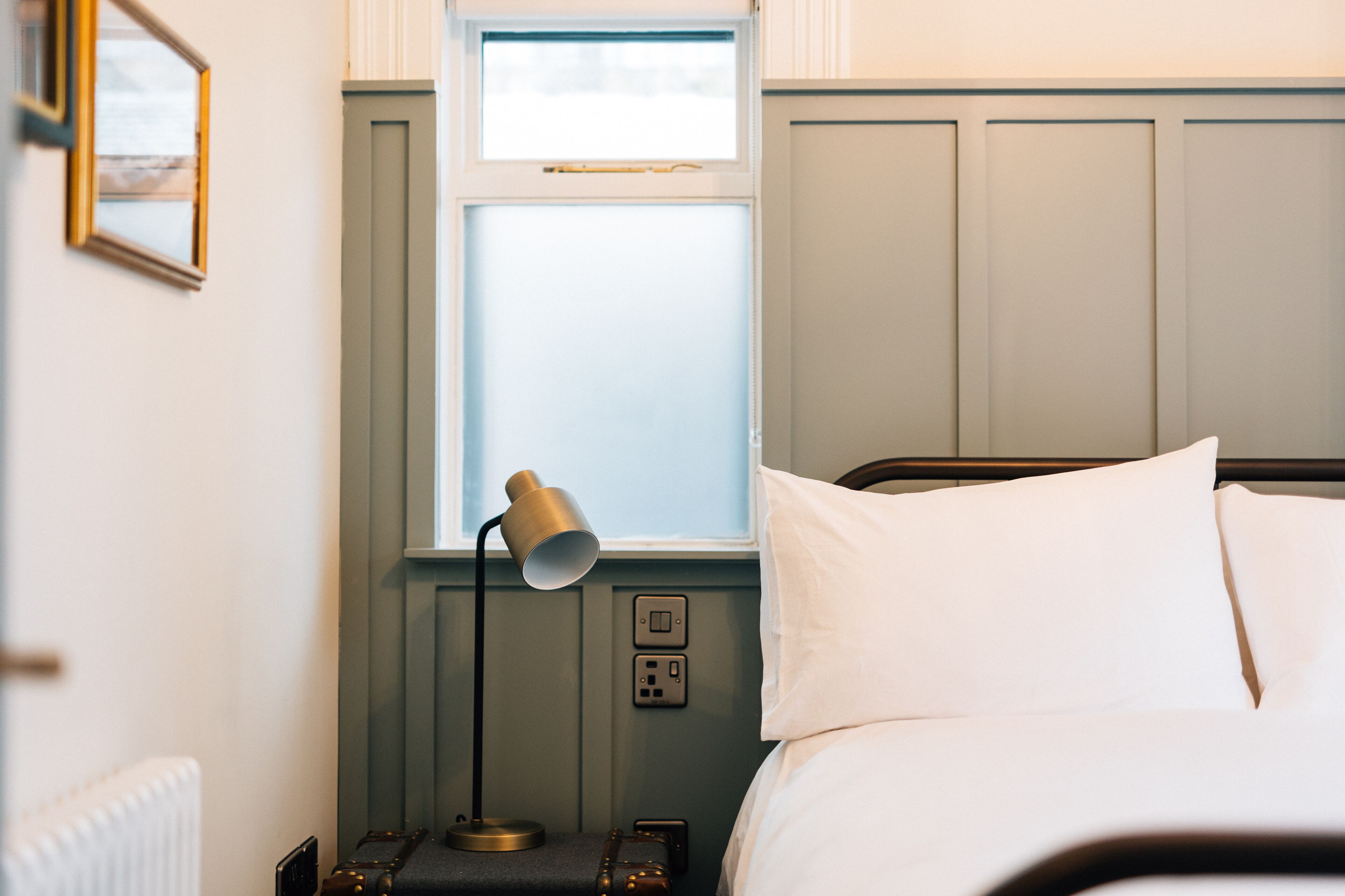 A neatly made bed with white linens, a bedside lamp, and a window with a view.