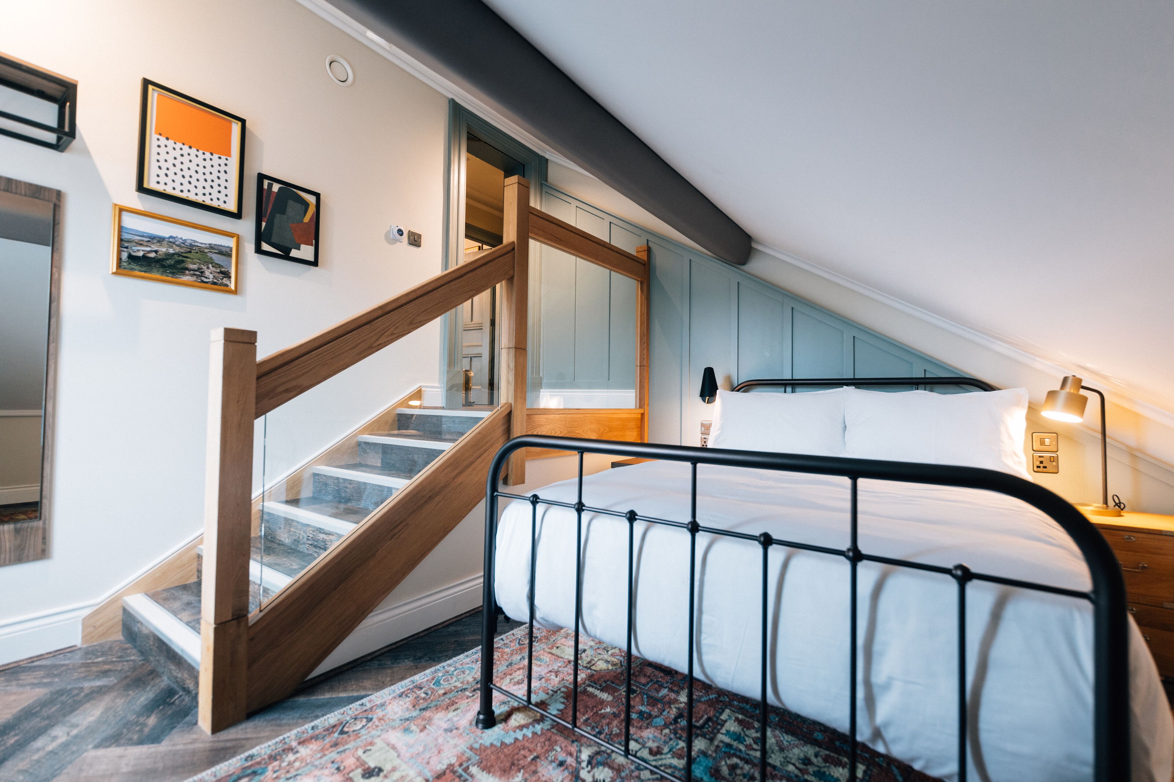 A bedroom with a bed, a wooden staircase, and a view of the hallway.