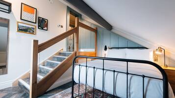 A bedroom with a bed, a wooden staircase, and a view of the hallway.