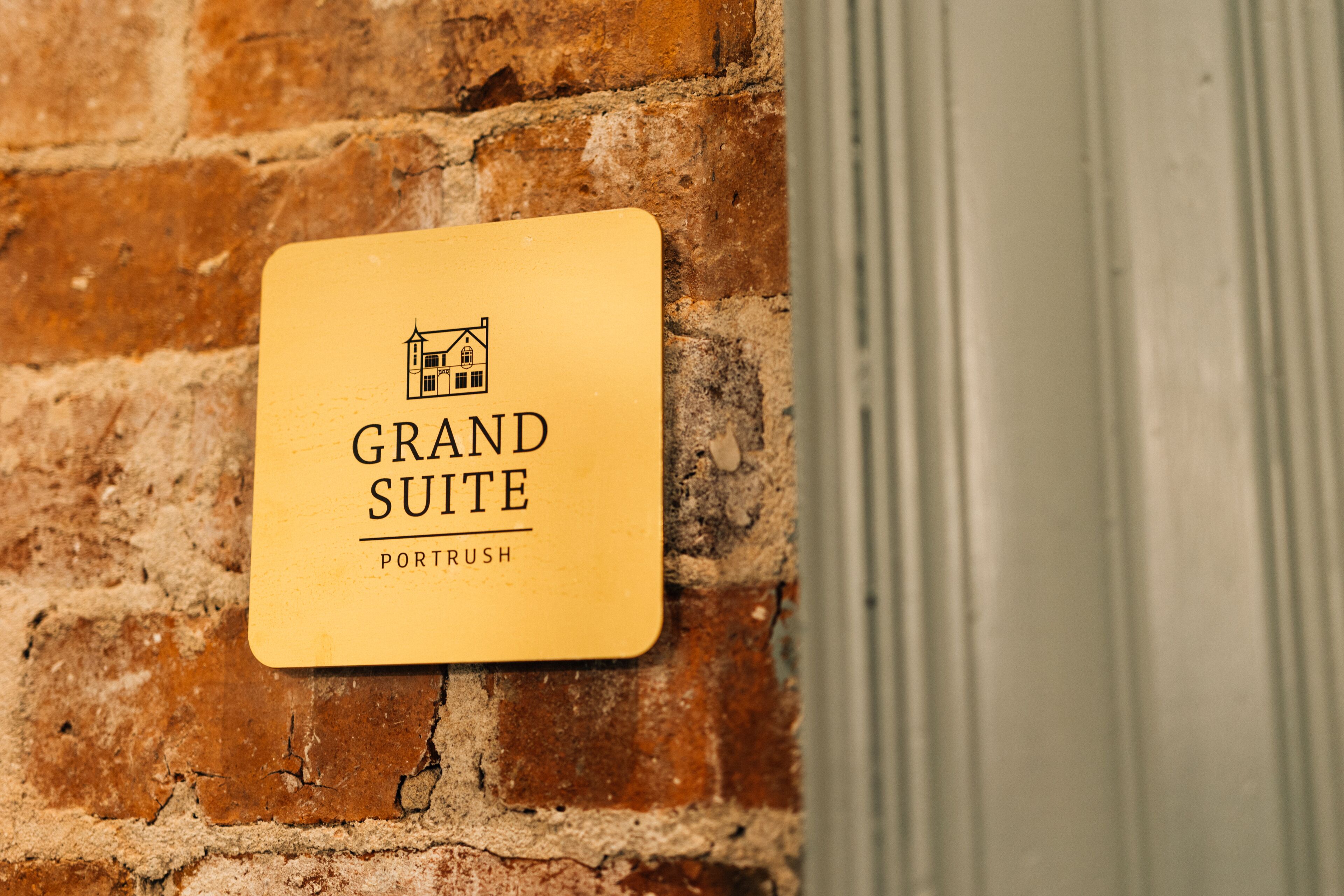 A sign on a brick wall that reads "Grand Suite" with a small house icon and the word "Port Rush" below it.