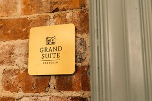 A sign on a brick wall that reads "Grand Suite" with a small house icon and the word "Port Rush" below it. - Bank Apartments (Portrush)