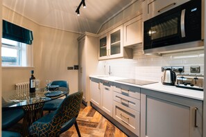 A modern kitchen with white cabinets, a microwave, and a toaster. There is a dining table with chairs and a bottle of wine. - Bank Apartments (Portrush)