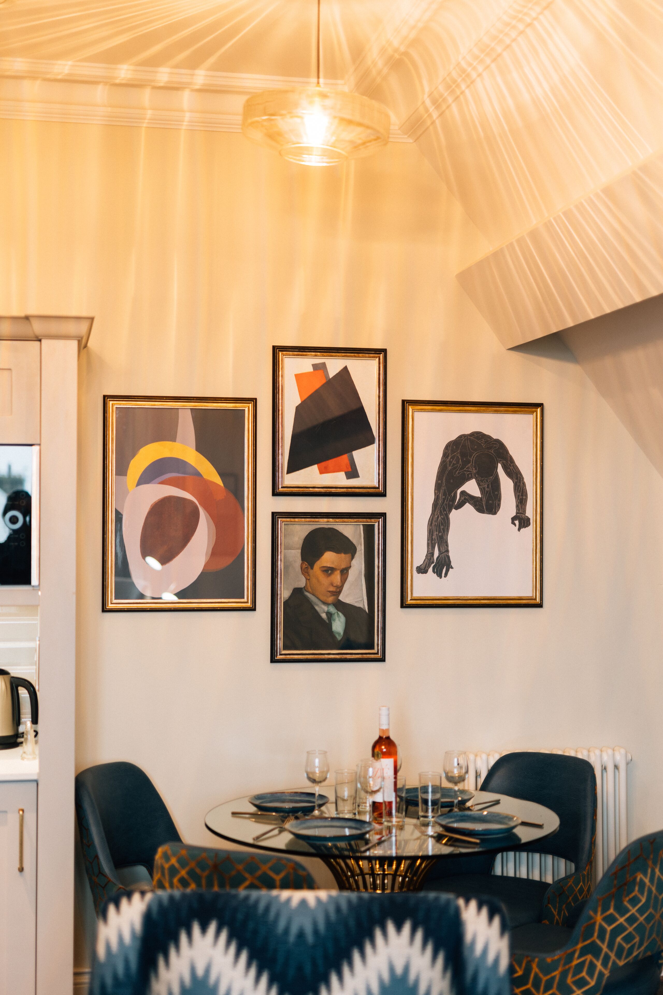 A dining area with a round table, chairs, and framed artwork on the wall.