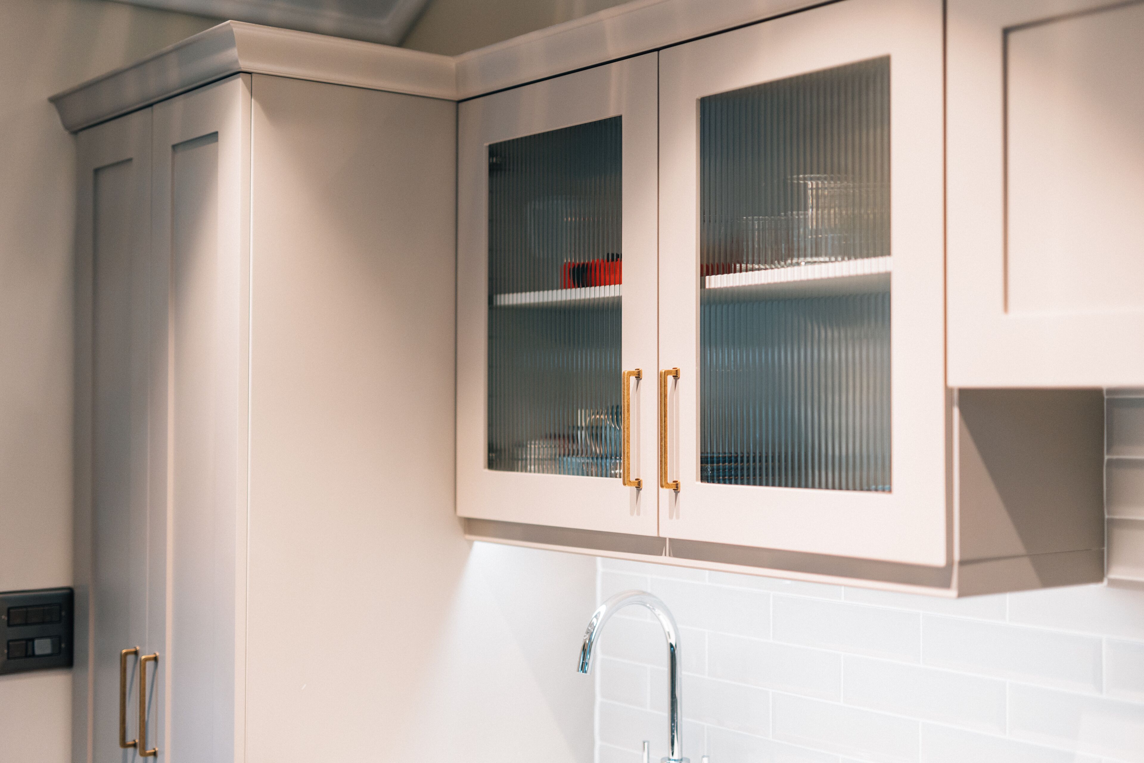Cucina con pensili bianchi, rubinetto in acciaio inossidabile e zoccolo a mosaico.