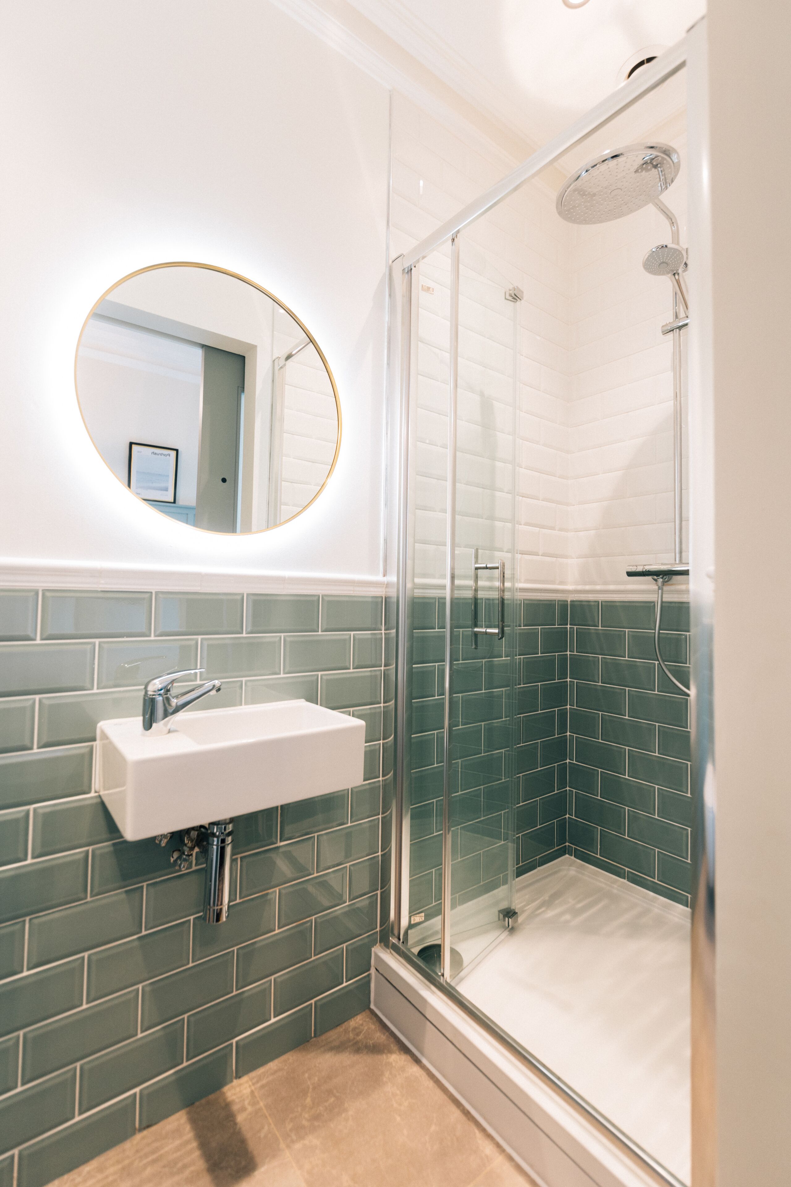 A modern bathroom with a glass-enclosed shower, a white sink, and a round mirror.