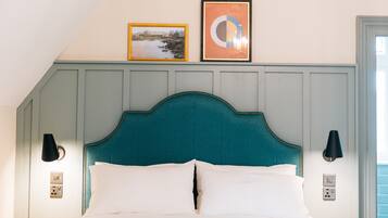 Ein ordentlich bezogenes Bett mit einem türkisfarbenen Kopfteil, zwei Wandleuchten und zwei gerahmte Bilder an der Wand darüber.