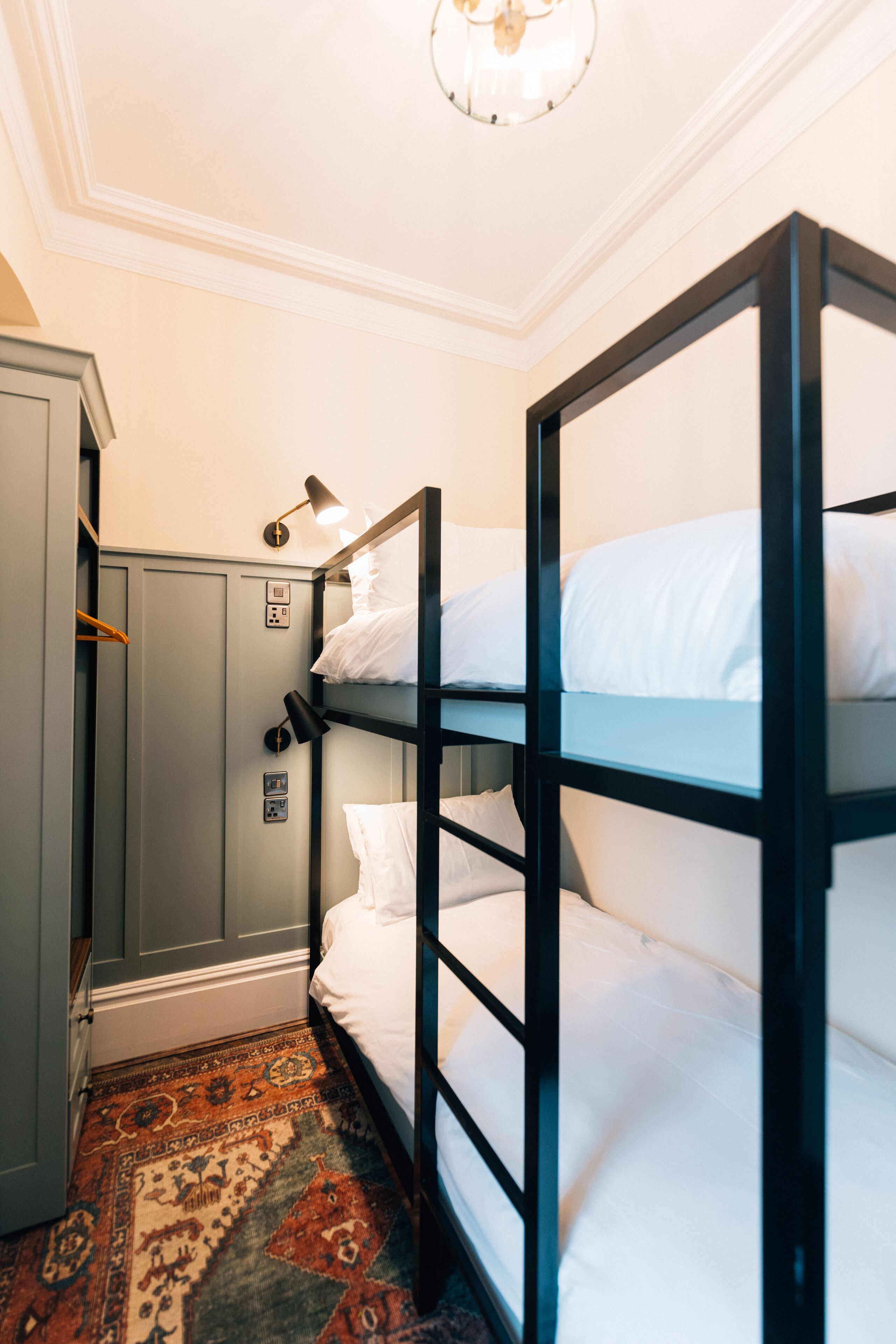 Habitación con literas, un escritorio, una lámpara, un tapete estampado y una lámpara de techo.