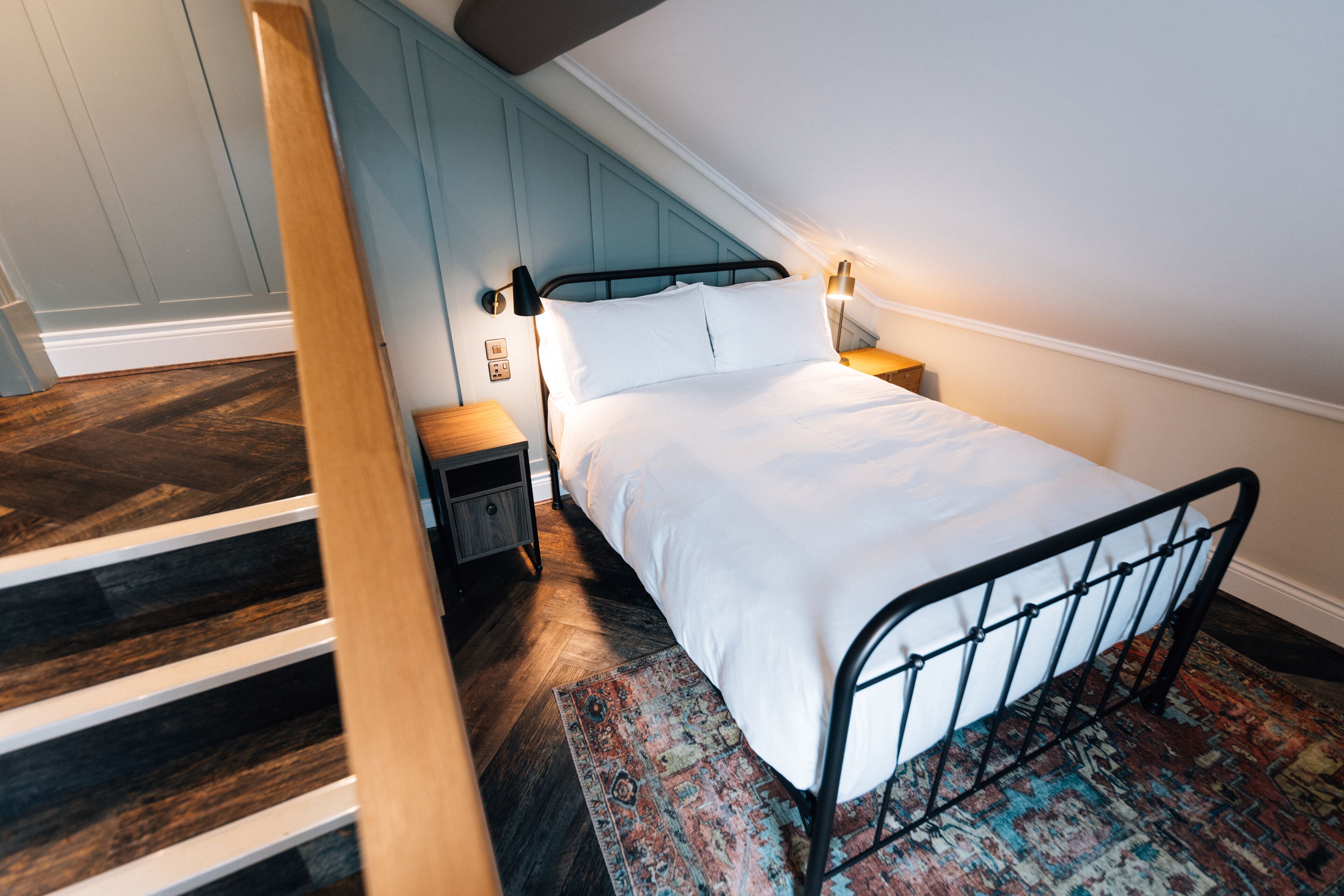 A bedroom with a bed, a nightstand, a lamp, and a patterned rug.