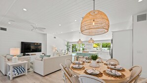 Una cocina moderna con una isla grande, armarios blancos y un comedor con sillas de mimbre y una mesa redonda para seis personas.