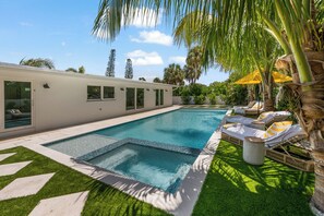 Un espace piscine moderne comprenant une piscine rectangulaire, un petit jacuzzi et des chaises longues.