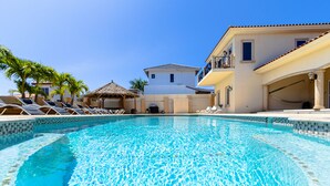 Una piscina con sillones reclinables y un edificio al fondo.