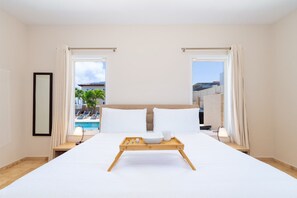 A hotel room with a large bed, a tray with breakfast items, and a view of a pool and buildings.