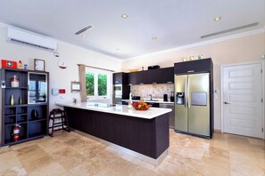 Une cuisine moderne dotée d’un îlot central, d’appareils électroménagers intégrés et offrant une vue sur l’extérieur.