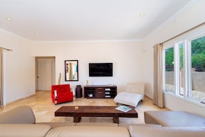 A spacious living room with a flat-screen TV mounted on the wall, a red chair, a white sofa, and a wooden coffee table. - Stunning 4BR Pool Villa w Patio near Palm Beach (Noord)
