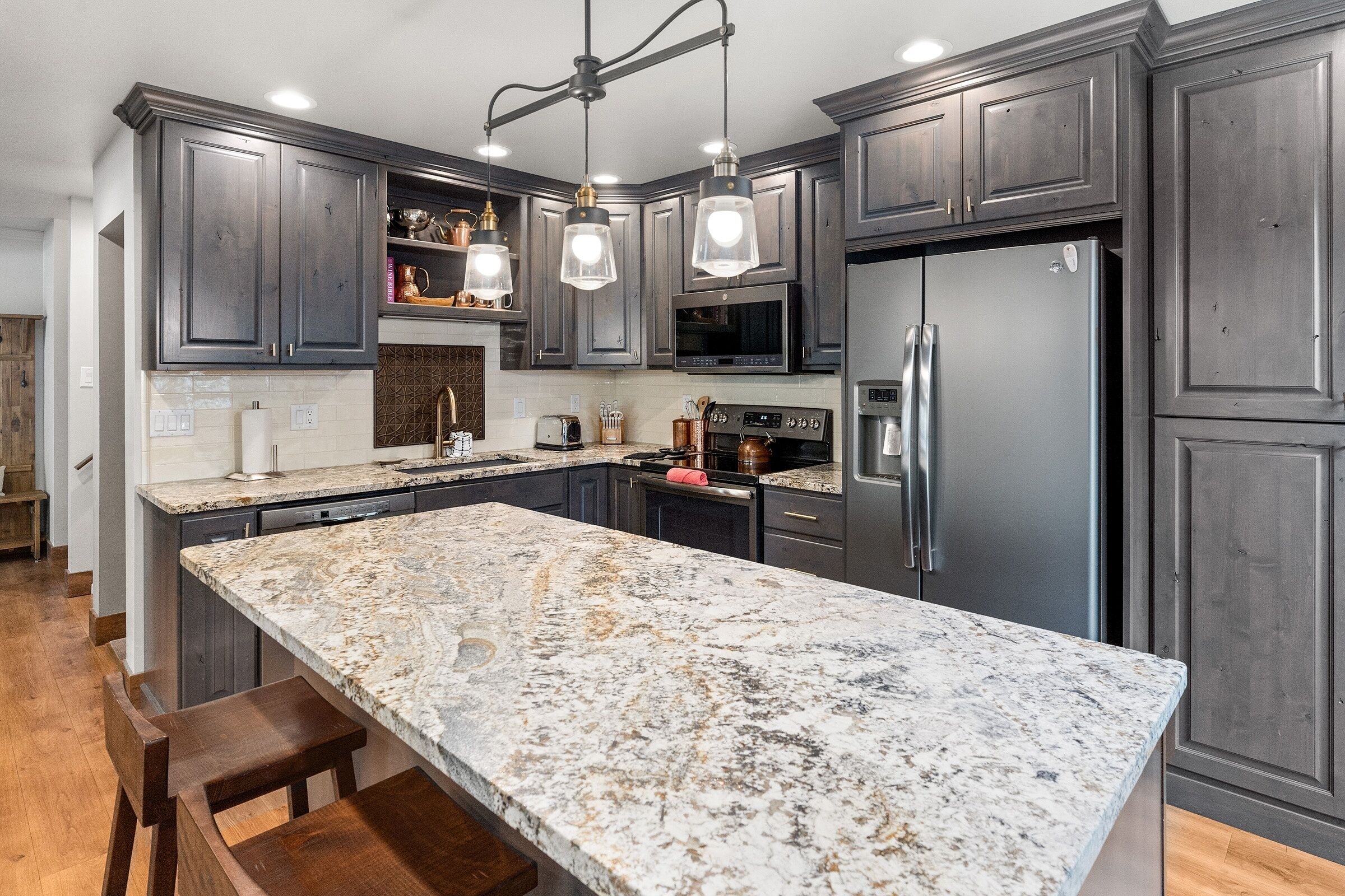 A modern kitchen with dark cabinetry, a large marble island, and stainless steel appliances.