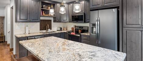 A modern kitchen with dark cabinetry, a large marble island, and stainless steel appliances.
