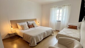 Een ruime slaapkamer met twee bedden, een groot raam met gordijnen, een flatscreen-tv aan de muur en een stoel.