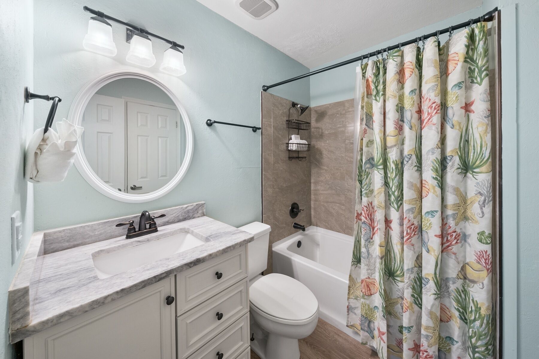 Un baño con lavamanos de mármol, inodoro, bañera y cortina de ducha con estampado floral.