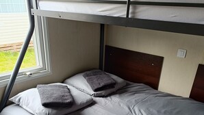 Ein Etagenbett grau bezogen, ein Fenster mit Jalousien und ein Holzboden.