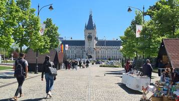 A cobblestone street with a large building in the background, a market stall on the right, and people walking.