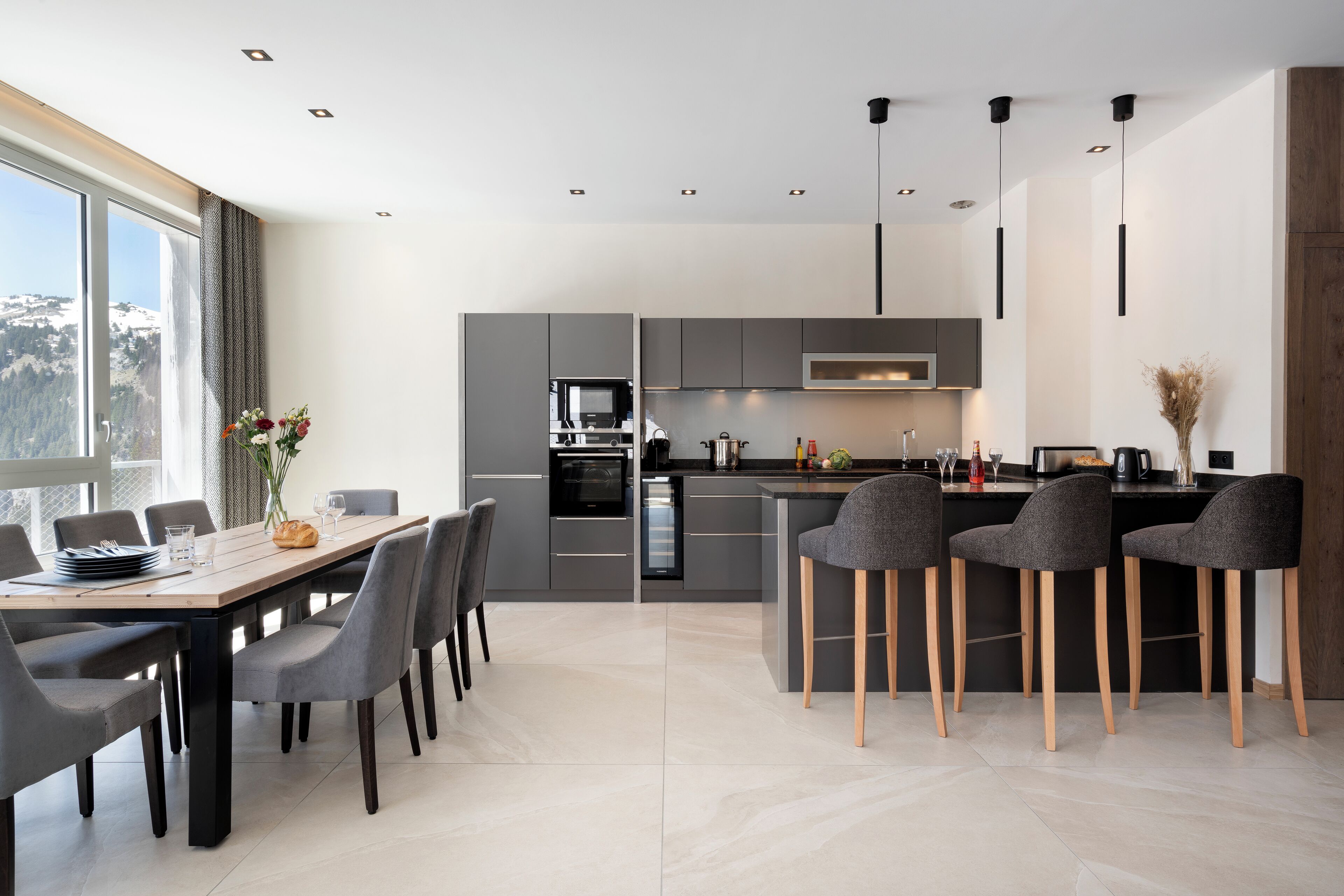 Una cucina moderna con mobili grigi, un'isola centrale con sgabelli da bar e un'area pranzo con un tavolo lungo e sedie.