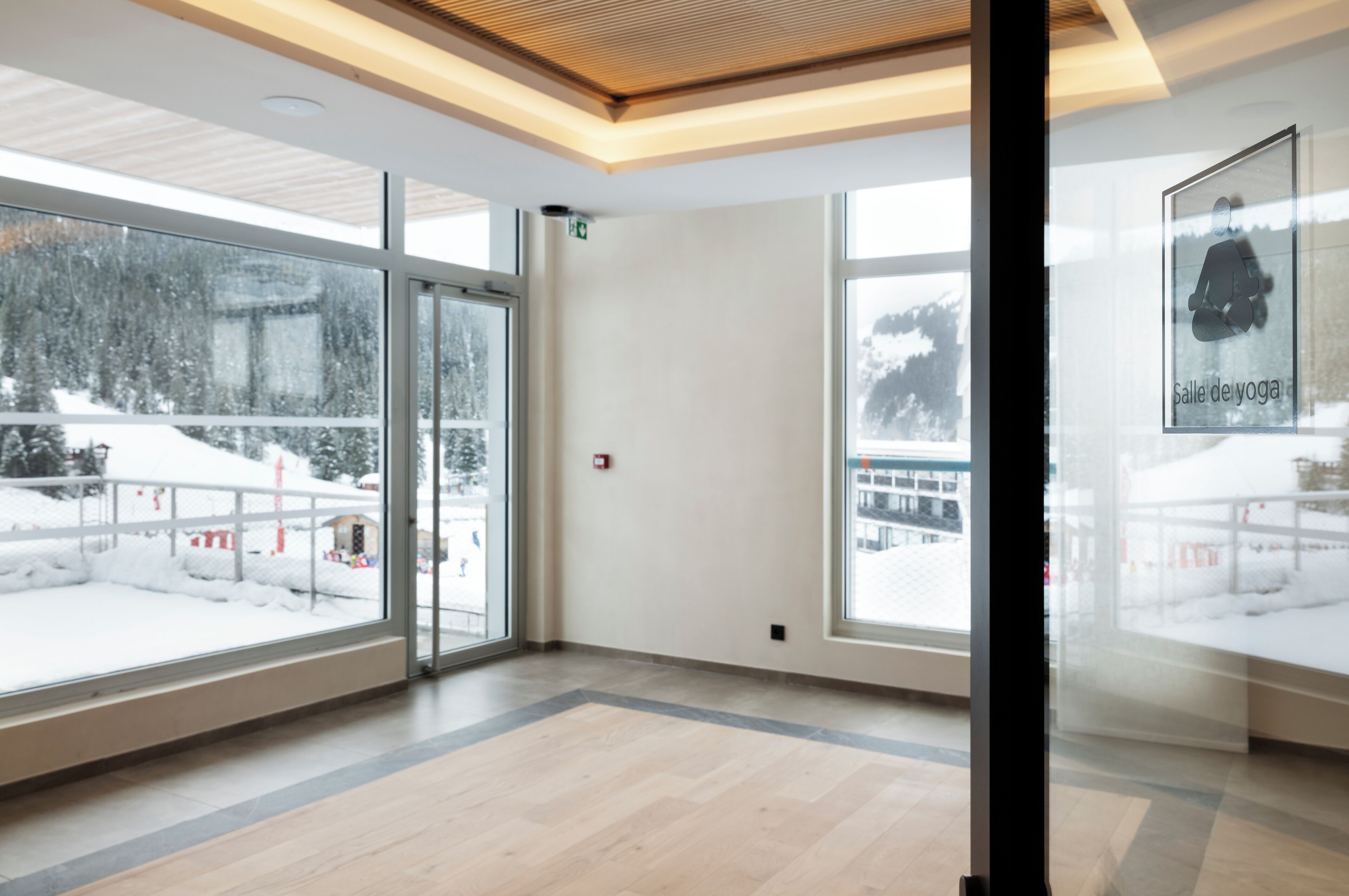 A modern interior with large windows, a wooden ceiling, and a framed yoga poster.