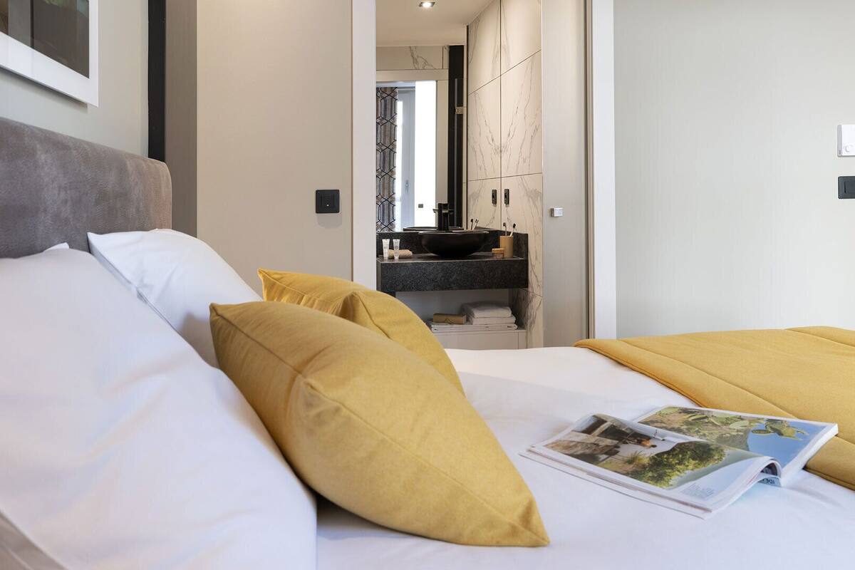 Habitación de hotel con cama, almohadas, una revista y baño visible a través de una puerta abierta.