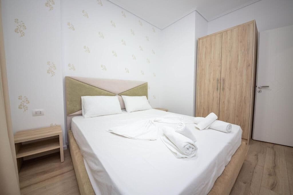 A neatly made bed with white linens and towels, a wooden headboard, and a wooden wardrobe.