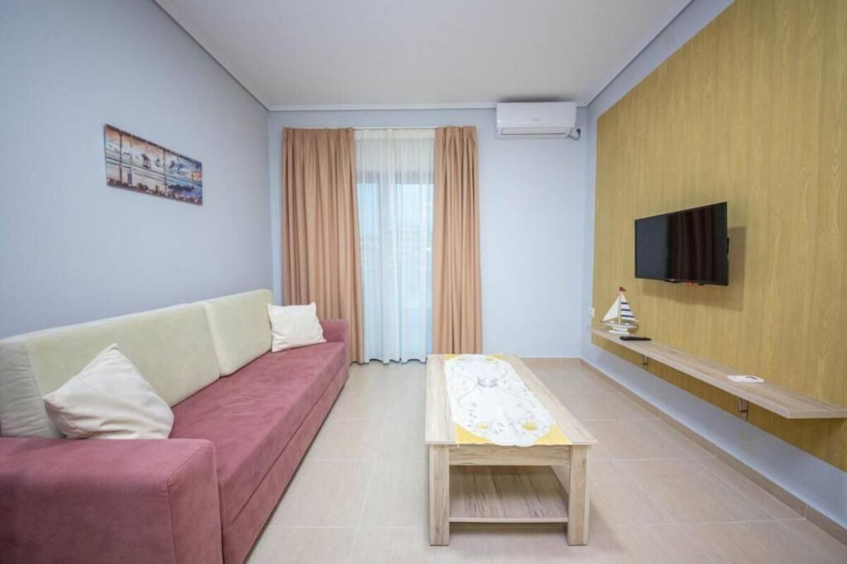 Una sala de estar con un sofá, una mesa de centro, un televisor montado en la pared y un ventanal con cortinas.