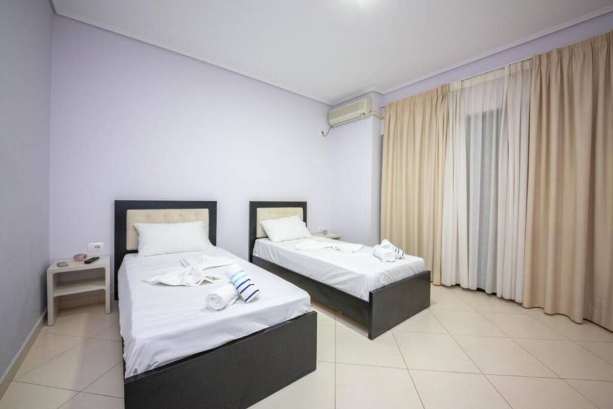 Una habitación de hotel con dos camas, una mesita de noche, una ventana con cortinas y un equipo de aire acondicionado.